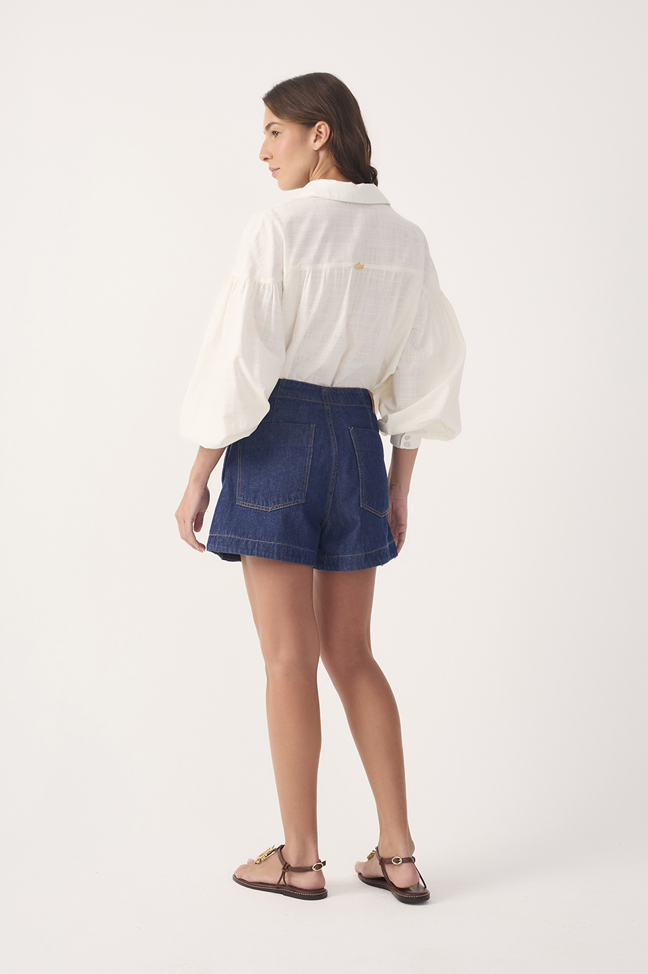 Model wearing dark blue denim topstitching shorts with a white blouse, full body back view showing pocket details