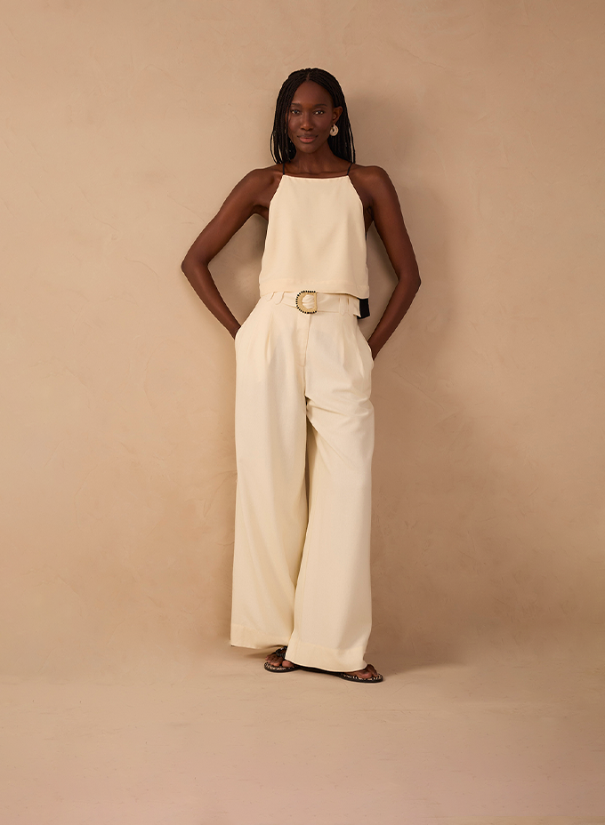 Woman wearing cream wide-leg pants with a halter top and gold belt from Dress To bottoms collection